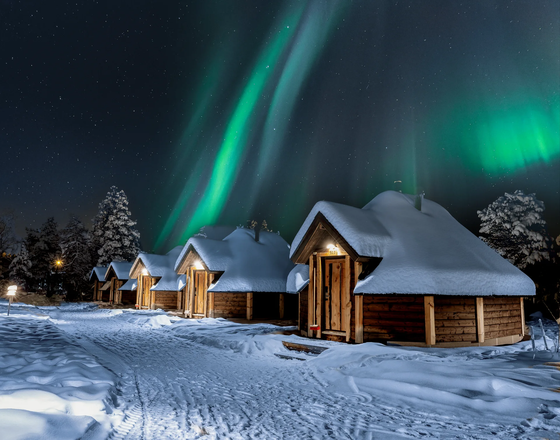 Aurora boreal iluminando o céu sobre cabanas de vidro em Inari